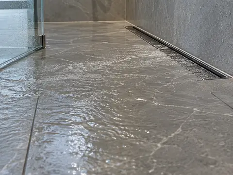 Пол душа из серого керамогранита с линейным трапом, по которому стекает вода